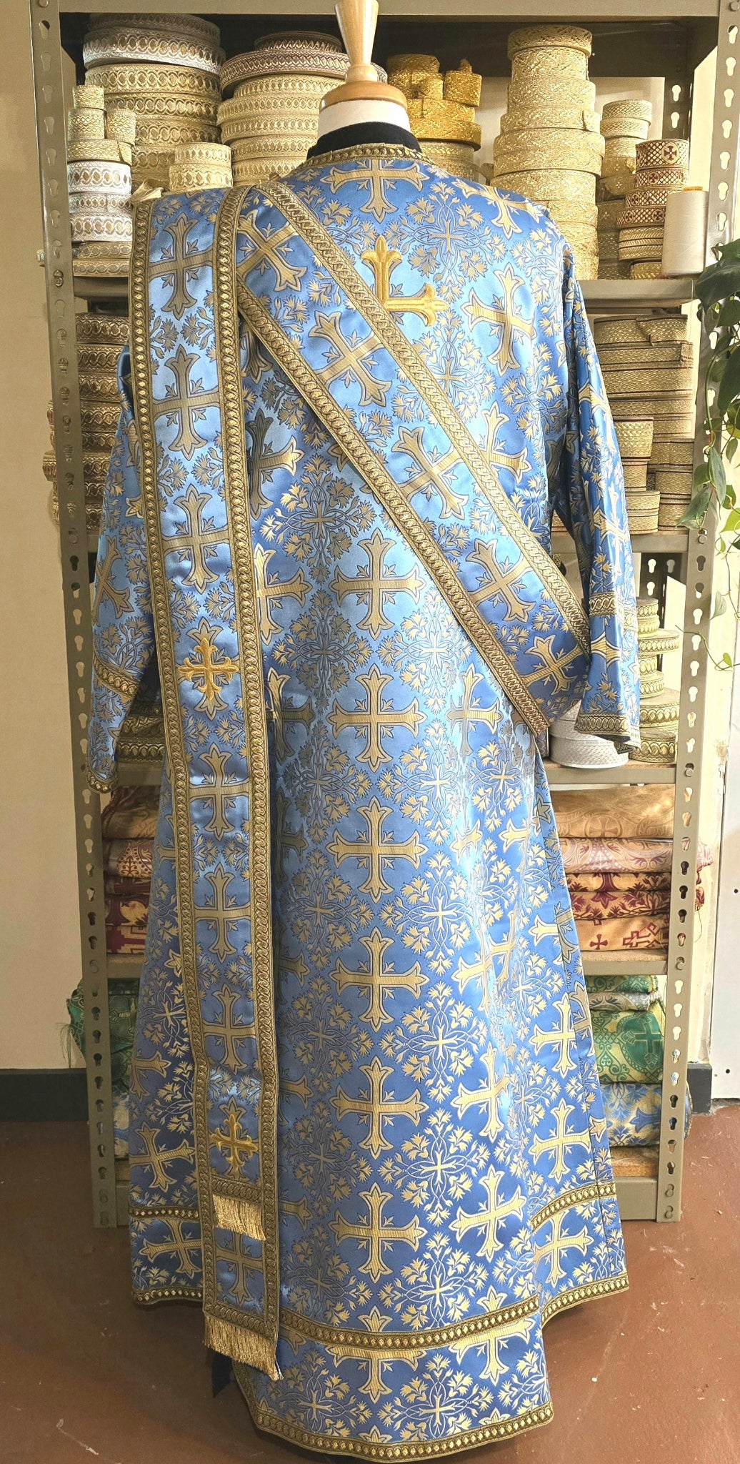Blue religious robe with gold embroidery on a mannequin against a blurred indoor background