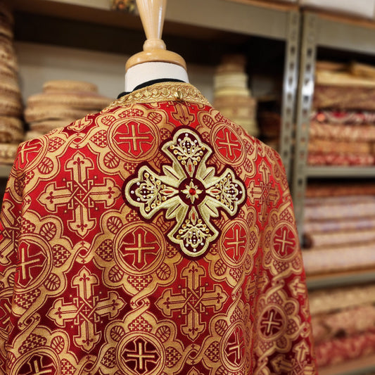Red and gold embroidered religious vestment on a mannequin against a fabric store background.